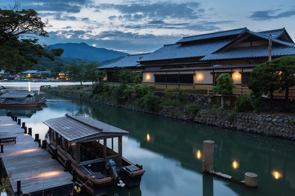 Katsura River bank with pleasure boat and illuminated building at sunset, Kyoto, Japan